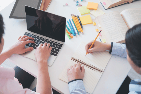 An image of people working on a desk, with a laptop and notebook - to represent our program to support middle school and high school homeschoolers.